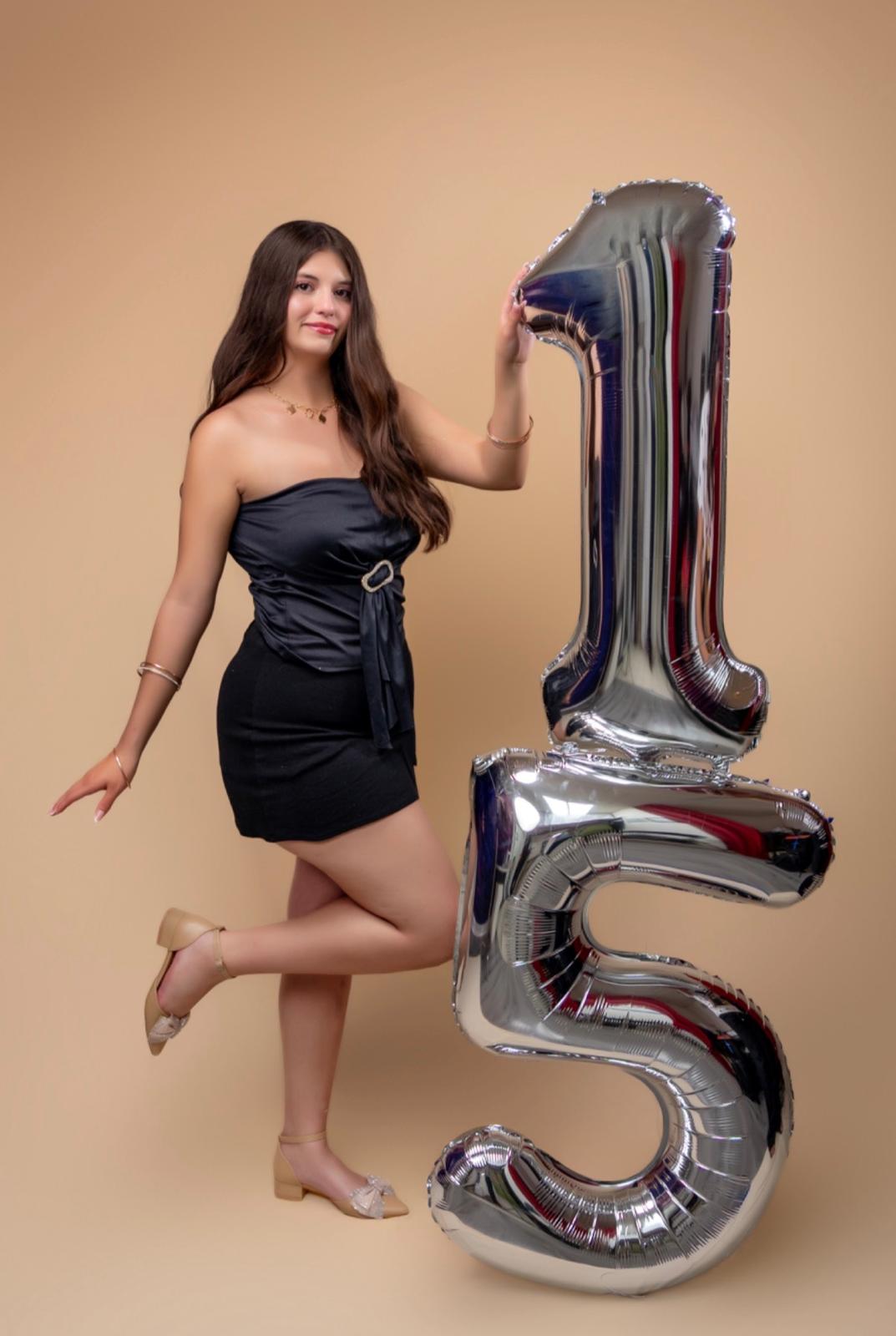 Karolina posando junto a globos plateados del número quince